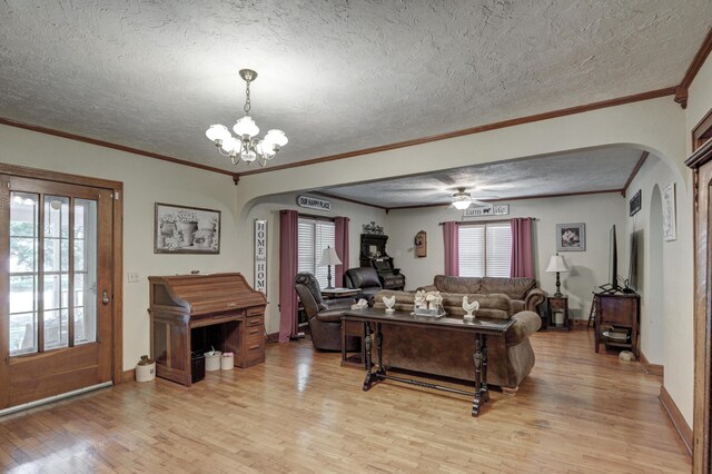 living room with ceiling fan with notable chandelier, light hardwood / wood-style floors, ornamental molding, and a textured ceiling