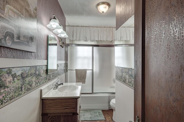 full bathroom featuring hardwood / wood-style floors, toilet, bath / shower combo with glass door, and vanity