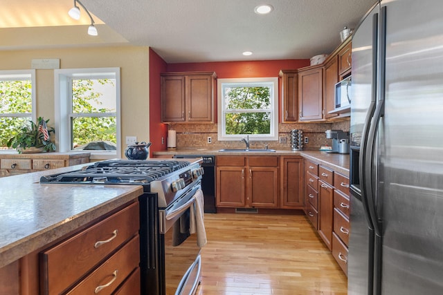 kitchen with plenty of natural light, light hardwood / wood-style floors, sink, stainless steel appliances, and backsplash