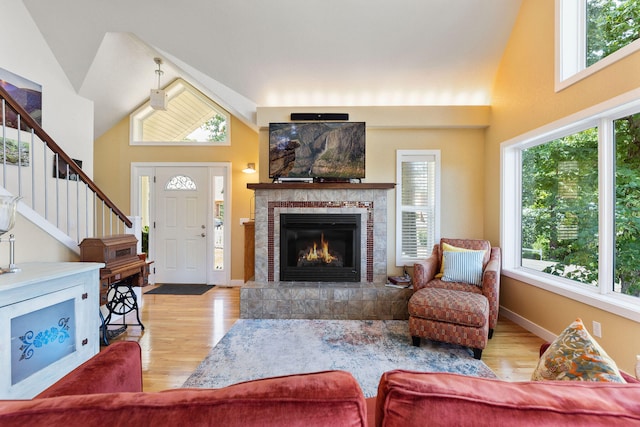 living room with high vaulted ceiling, a wealth of natural light, a tile fireplace, and light hardwood / wood-style floors