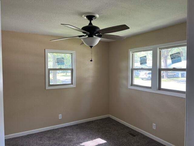 empty room featuring ceiling fan, dark colored carpet, and a wealth of natural light