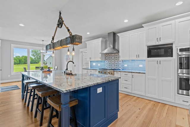 kitchen with a kitchen island with sink, wall chimney exhaust hood, light hardwood / wood-style floors, white cabinetry, and appliances with stainless steel finishes