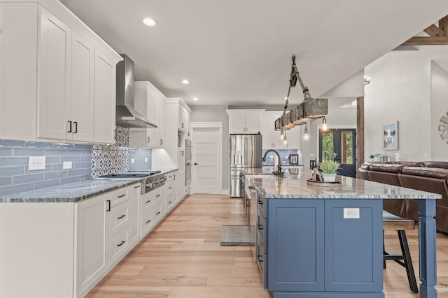 kitchen with a breakfast bar, white cabinets, light hardwood / wood-style floors, wall chimney range hood, and appliances with stainless steel finishes