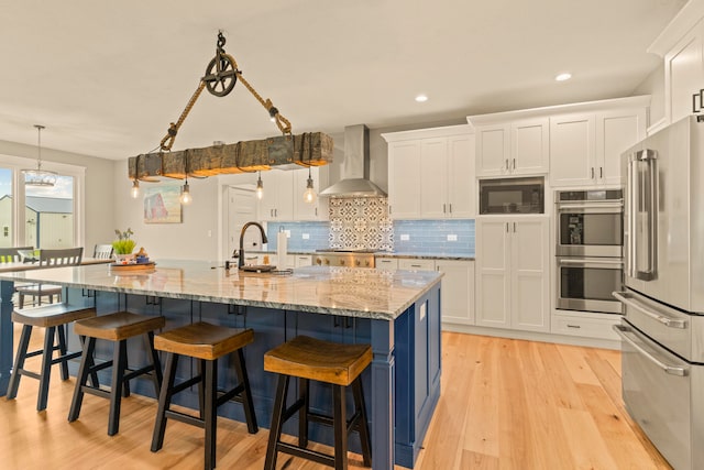 kitchen with stainless steel appliances, wall chimney exhaust hood, hanging light fixtures, white cabinetry, and a spacious island