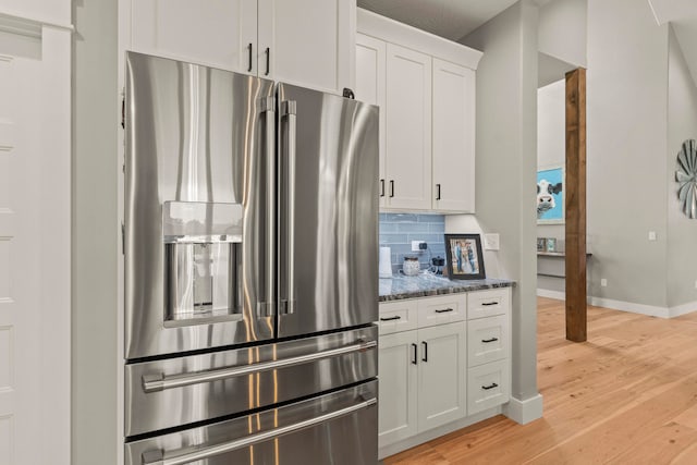 kitchen with dark stone countertops, white cabinets, stainless steel fridge with ice dispenser, and light wood-type flooring