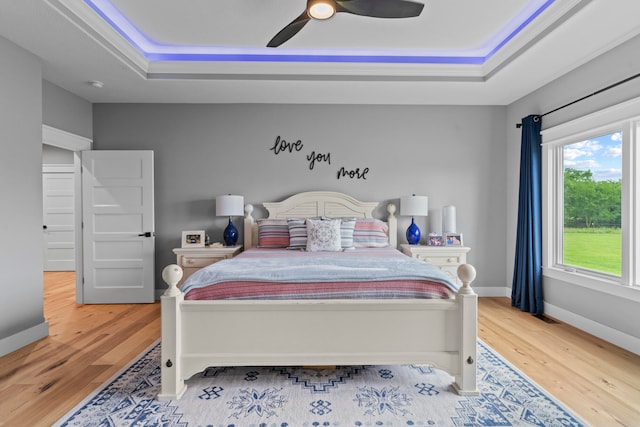 bedroom with ceiling fan, light hardwood / wood-style floors, and a raised ceiling