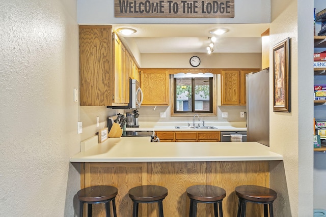 kitchen with brown cabinets, a textured wall, a sink, a peninsula, and appliances with stainless steel finishes