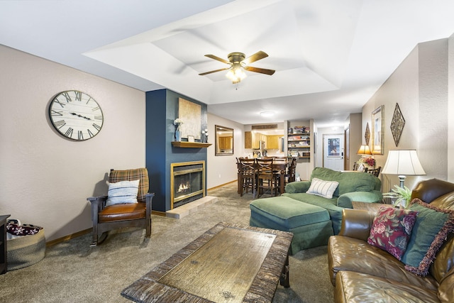 living room featuring a large fireplace, a tray ceiling, carpet flooring, and ceiling fan