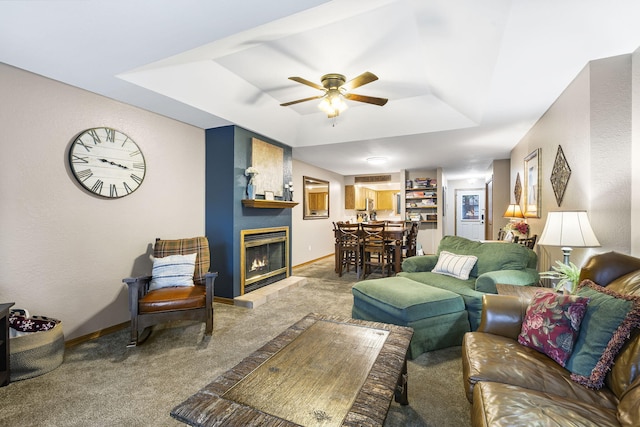 living room with a fireplace, a tray ceiling, carpet floors, and ceiling fan