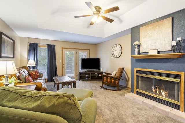 living room with a raised ceiling, ceiling fan, light colored carpet, and a tiled fireplace