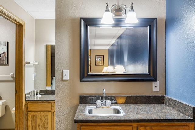 bathroom featuring a textured wall, toilet, and vanity