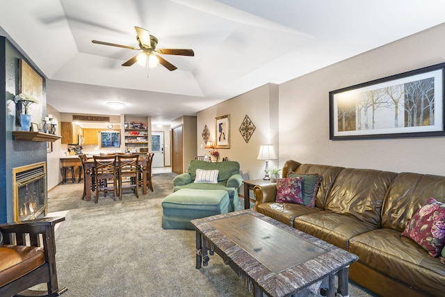 carpeted living room with a tray ceiling, a fireplace, and ceiling fan