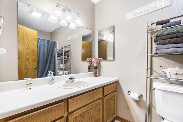 full bath with toilet, a textured wall, and vanity