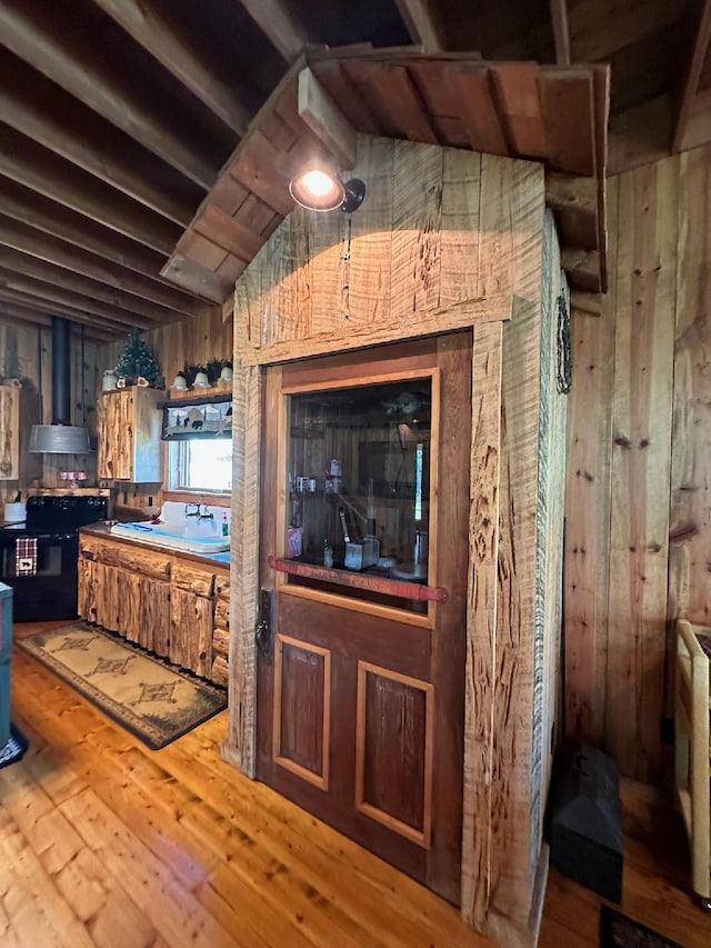 kitchen featuring wall chimney exhaust hood, hardwood / wood-style floors, black electric range, and wooden walls