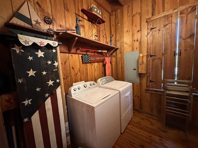 clothes washing area with electric panel, hardwood / wood-style floors, wooden walls, and washer and clothes dryer