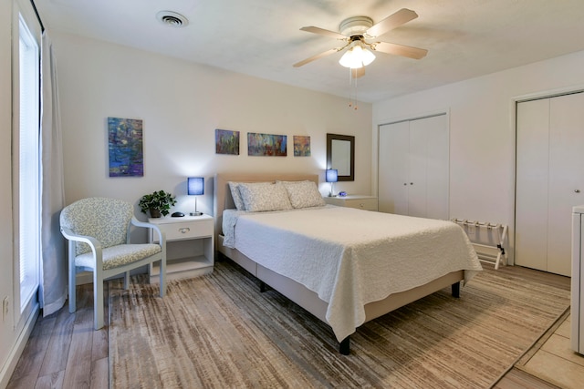 bedroom with hardwood / wood-style floors, two closets, and ceiling fan