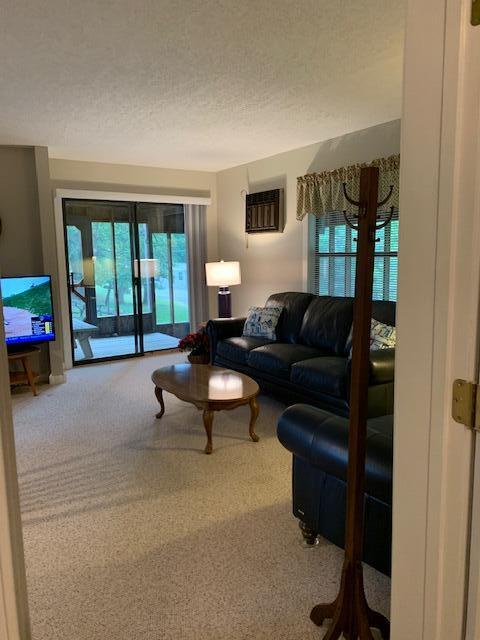 living room featuring a textured ceiling, carpet flooring, and a wall unit AC