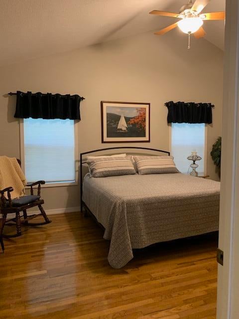 bedroom with ceiling fan, hardwood / wood-style floors, and vaulted ceiling