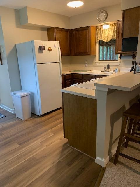 kitchen with white refrigerator, kitchen peninsula, and light hardwood / wood-style flooring