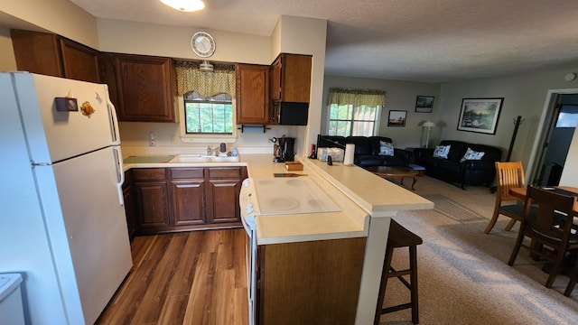 kitchen with white appliances, dark hardwood / wood-style flooring, a kitchen breakfast bar, kitchen peninsula, and a textured ceiling