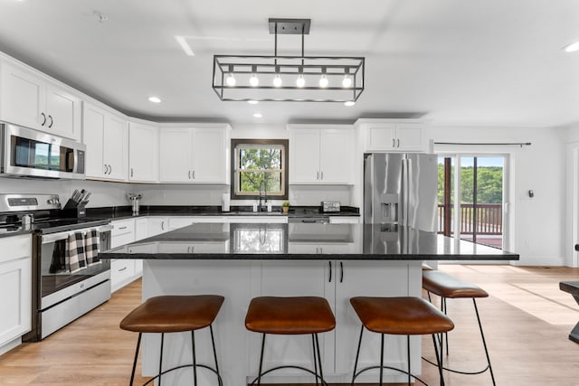 kitchen with stainless steel appliances, decorative light fixtures, a kitchen island, and light wood-type flooring