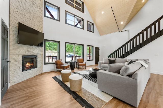 living room featuring a high ceiling, light hardwood / wood-style floors, a stone fireplace, and wood ceiling