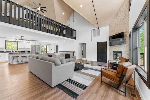 living room with light hardwood / wood-style floors, wood ceiling, sink, a stone fireplace, and high vaulted ceiling