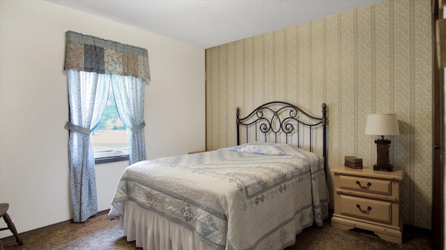 bedroom with dark colored carpet, a textured ceiling, baseboards, and wallpapered walls