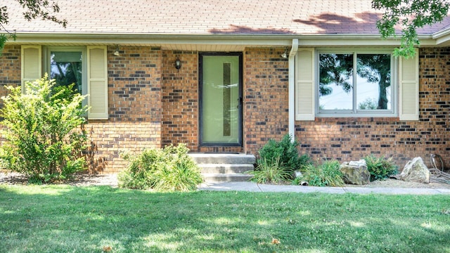 entrance to property featuring brick siding and a lawn