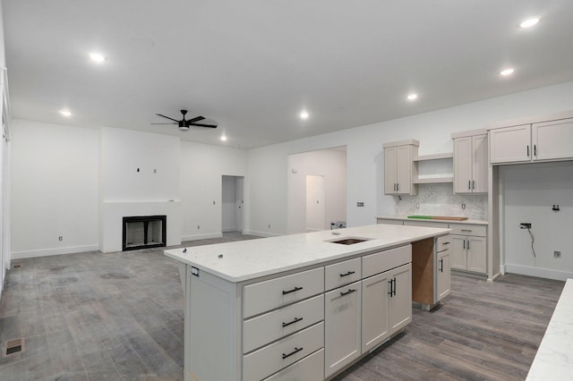 kitchen featuring white cabinetry, a center island, ceiling fan, light stone counters, and decorative backsplash