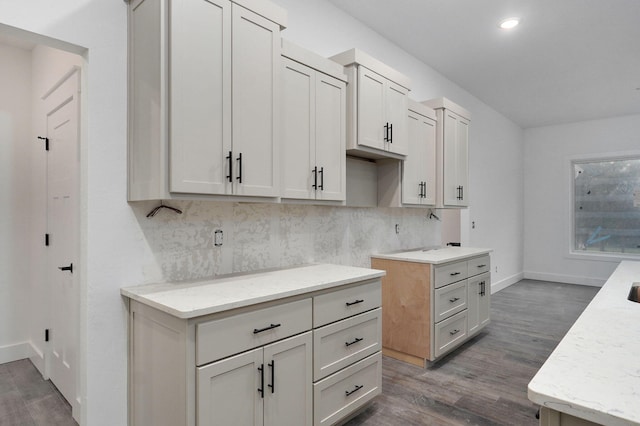 kitchen with white cabinets, dark hardwood / wood-style flooring, light stone countertops, and tasteful backsplash