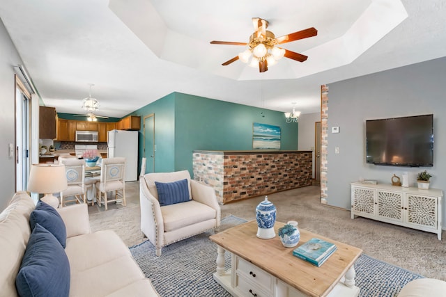 carpeted living room featuring ceiling fan with notable chandelier and a tray ceiling