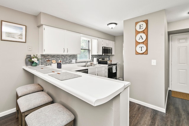 kitchen with a kitchen bar, stainless steel appliances, kitchen peninsula, and white cabinetry