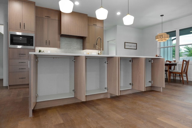 kitchen with stainless steel microwave, hanging light fixtures, light hardwood / wood-style floors, and sink