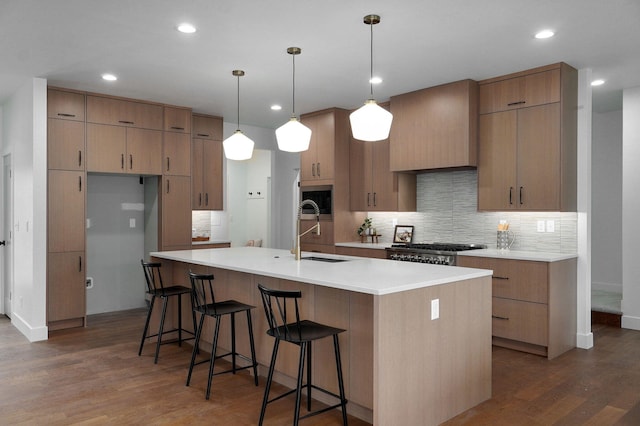 kitchen featuring a kitchen island with sink, sink, dark hardwood / wood-style flooring, hanging light fixtures, and backsplash