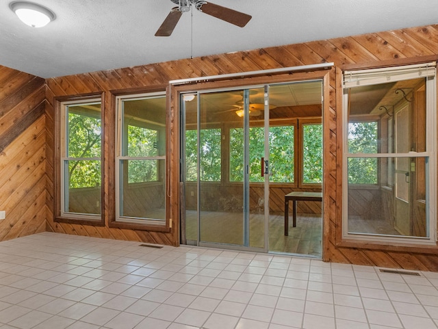 doorway to outside with a healthy amount of sunlight, ceiling fan, and wood walls