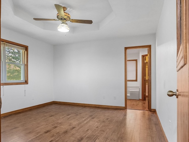 empty room with wood-type flooring, a tray ceiling, and ceiling fan