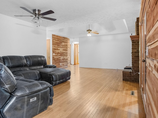 living room featuring ceiling fan, a brick fireplace, a textured ceiling, wooden walls, and hardwood / wood-style flooring