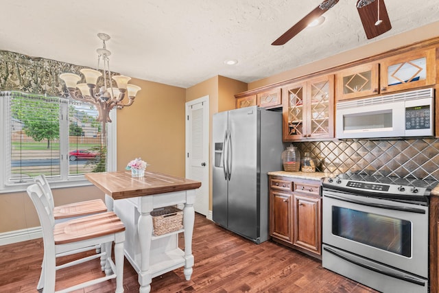 kitchen featuring tasteful backsplash, dark wood-type flooring, ceiling fan with notable chandelier, appliances with stainless steel finishes, and decorative light fixtures