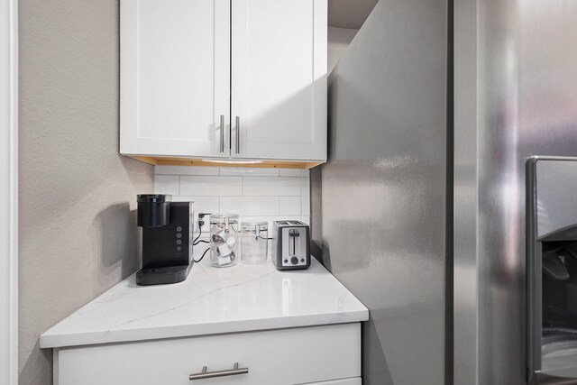 kitchen featuring stainless steel fridge, light stone counters, backsplash, and white cabinets