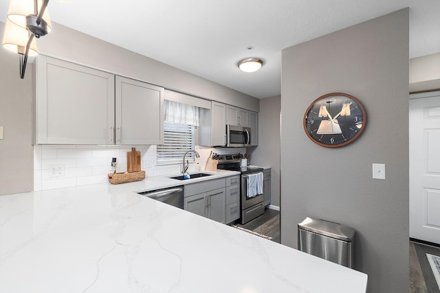 kitchen featuring light stone counters, sink, gray cabinetry, dark wood-type flooring, and appliances with stainless steel finishes