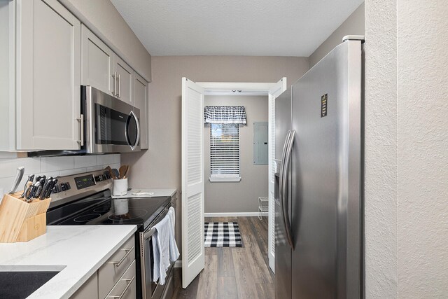 kitchen featuring electric panel, a textured ceiling, stainless steel appliances, light stone countertops, and dark hardwood / wood-style flooring