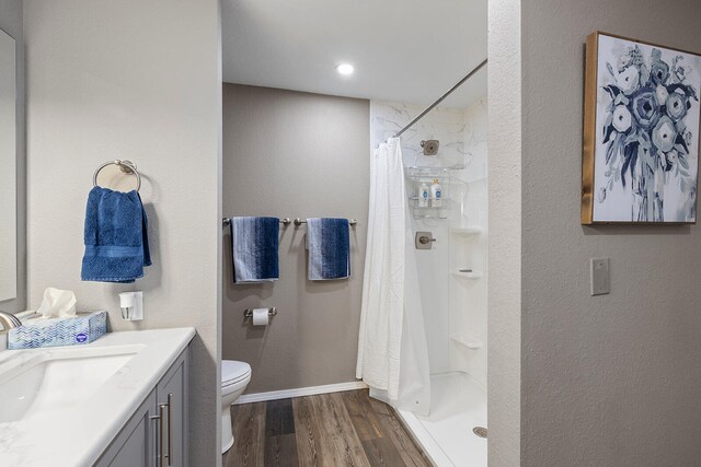 bathroom with hardwood / wood-style floors, toilet, walk in shower, and vanity