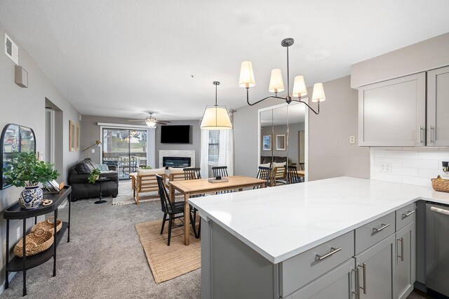 kitchen with gray cabinetry, light colored carpet, decorative light fixtures, light stone countertops, and kitchen peninsula