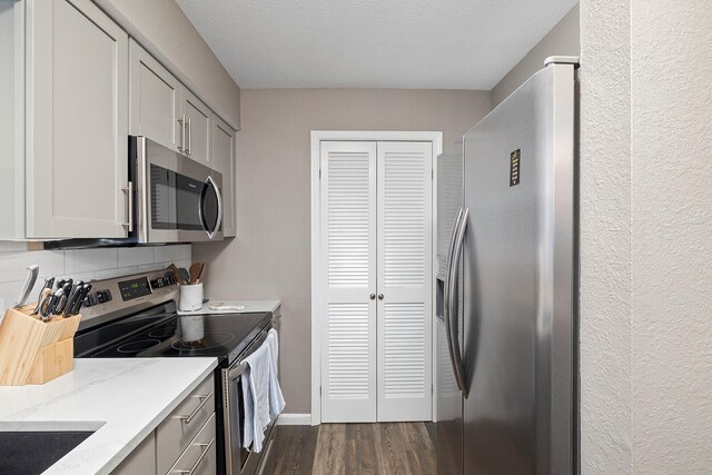 kitchen with light stone countertops, dark hardwood / wood-style floors, appliances with stainless steel finishes, and a textured ceiling