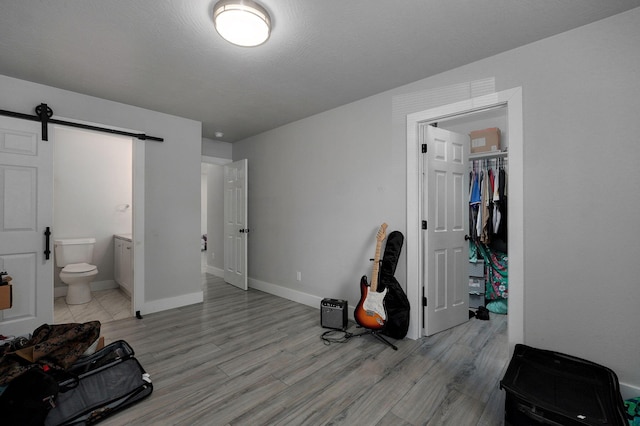 bedroom featuring a barn door, a closet, light wood-type flooring, and ensuite bath