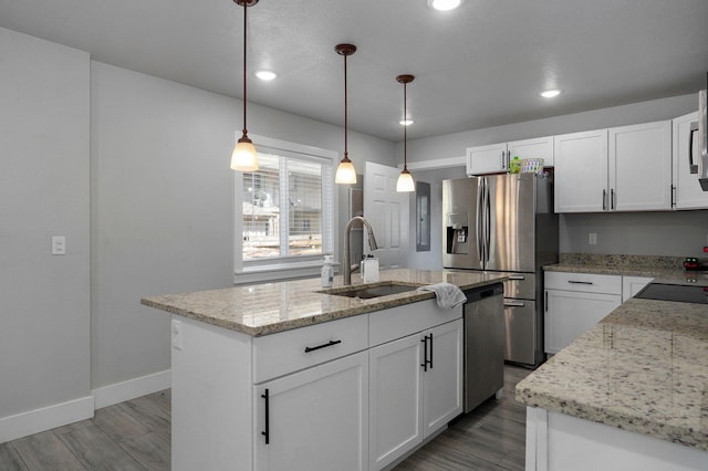 kitchen with light stone counters, pendant lighting, an island with sink, white cabinets, and sink