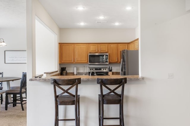 kitchen with stainless steel appliances, kitchen peninsula, light colored carpet, and a breakfast bar