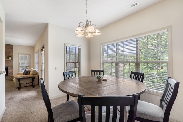dining space featuring a stone fireplace, visible vents, baseboards, light colored carpet, and a notable chandelier