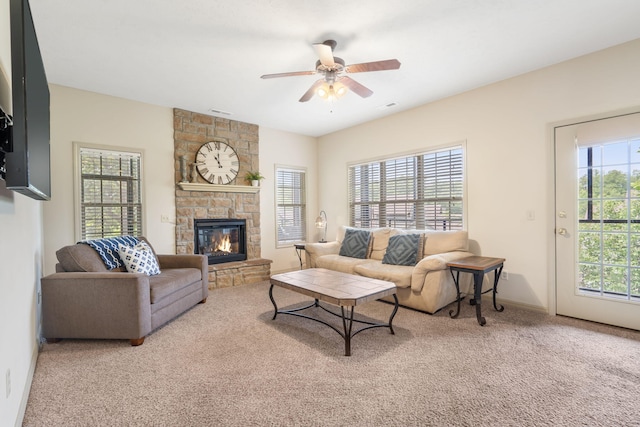 carpeted living area with baseboards, a stone fireplace, and ceiling fan
